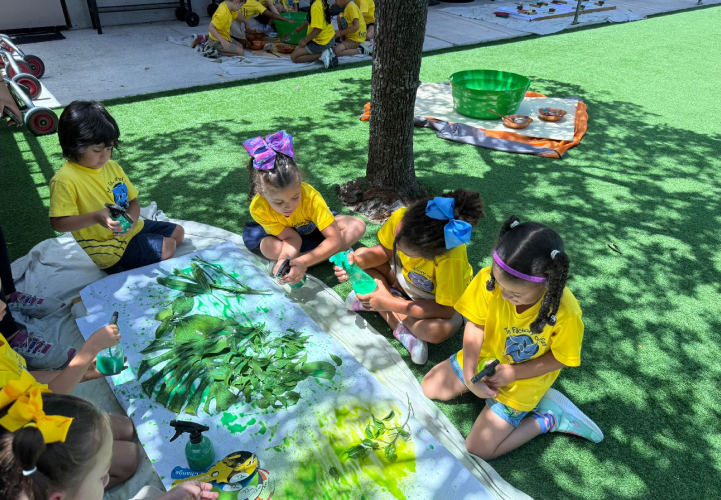 Preschool children engaged in an outdoor nature inspired art project using spray bottles and leaves at Brickell International Academy in Miami