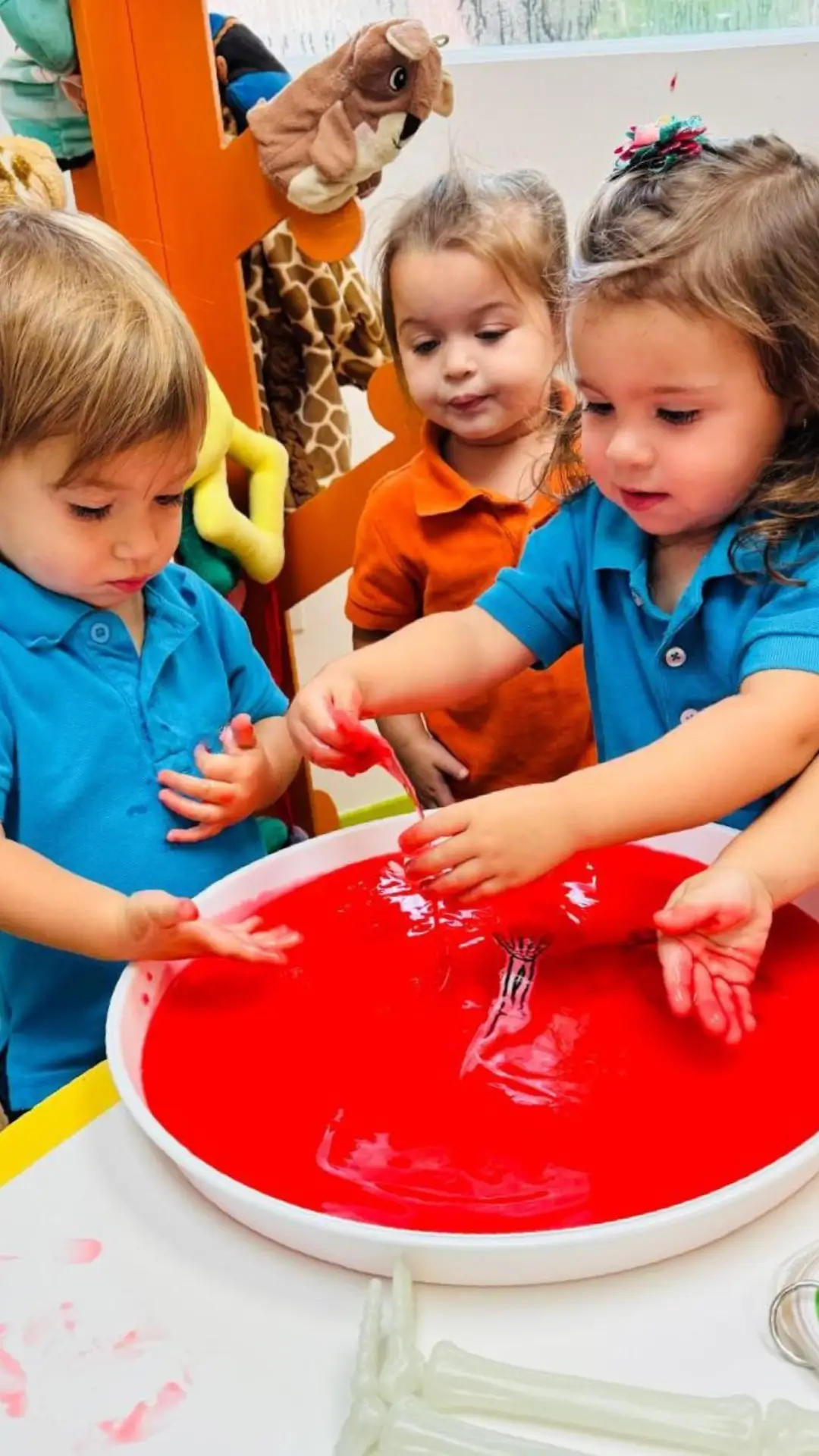 Toddlers participating in a hands on sensory play activity with red slime at Brickell International Academy preschool in Miami